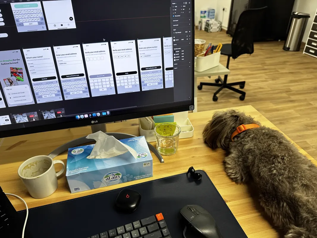 A desk with Figma open on the monitor and a dog sitting on the desk beside it